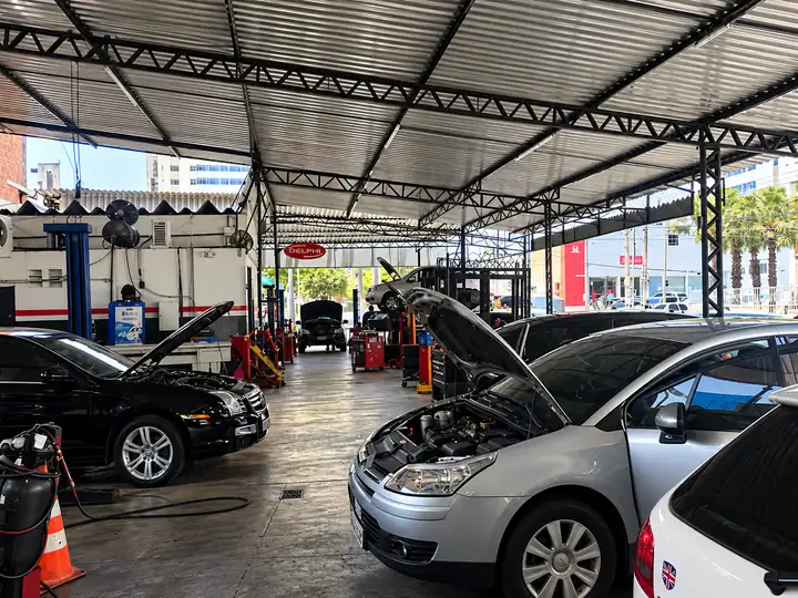 Carros em manutenção dentro da oficina Dom Victor, com o painel da Delphi ao fundo